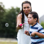 Pojke blåser såpbubblor tillsammans med kvinna i långt hår och flätor