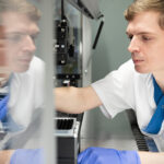 Man iklädd sjukhuskläder och handskar arbetar vid instrument på lab.