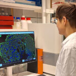 Kvinna i laboratorierock arbetar framför dator på lab.