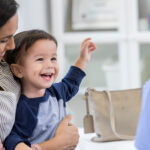 Leende barn i mammas knä träffar läkare.