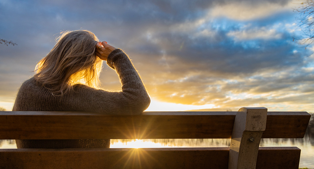 Kvinna på bänk tittar ut över solnedgång.